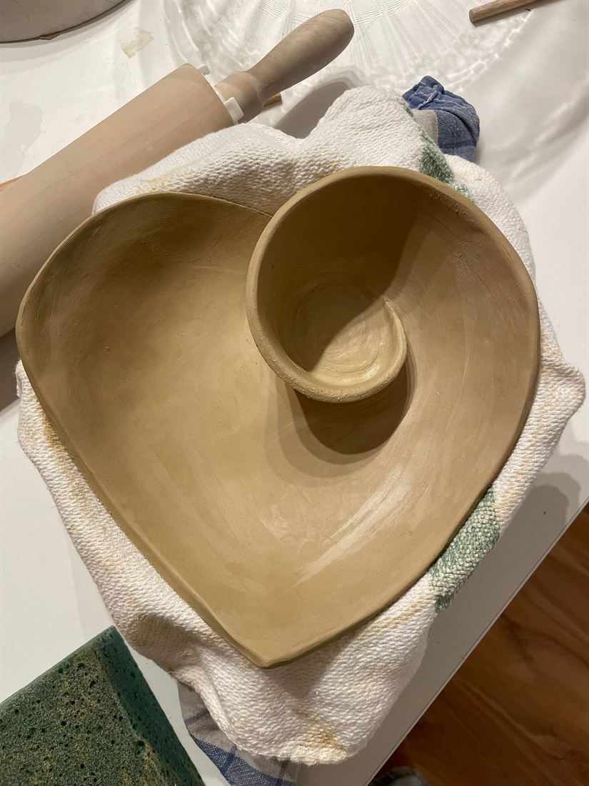 Herzförmige Schale mit eingerollter Spirale aus ungebranntem Ton auf einem Tuch